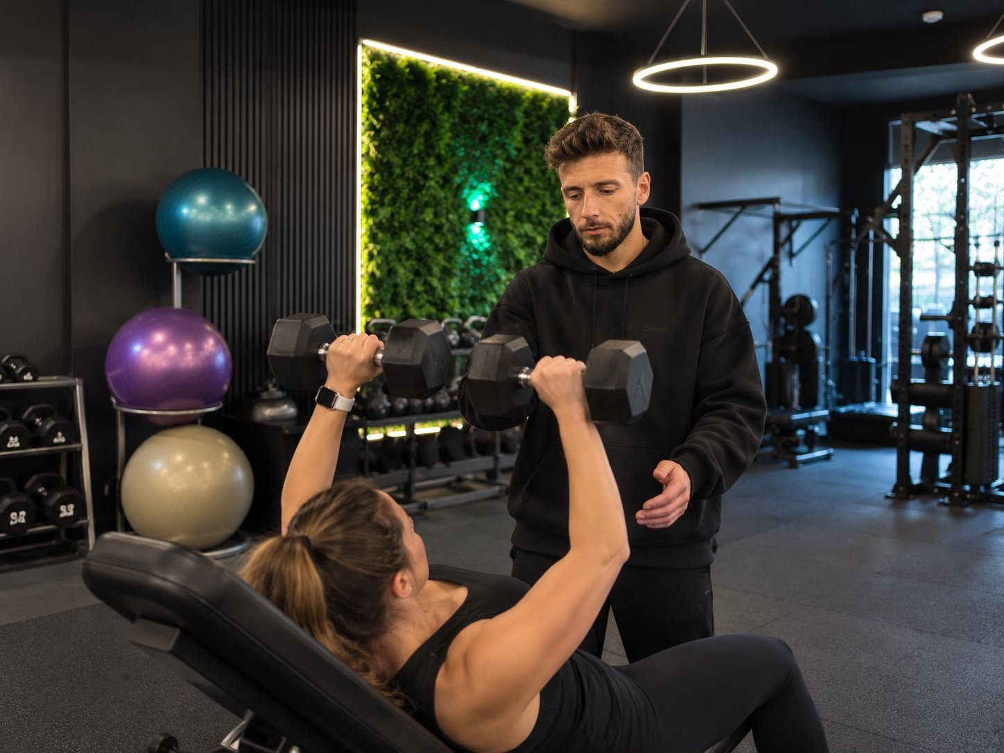 Personal trainer supporting a woman during a dumbbell press